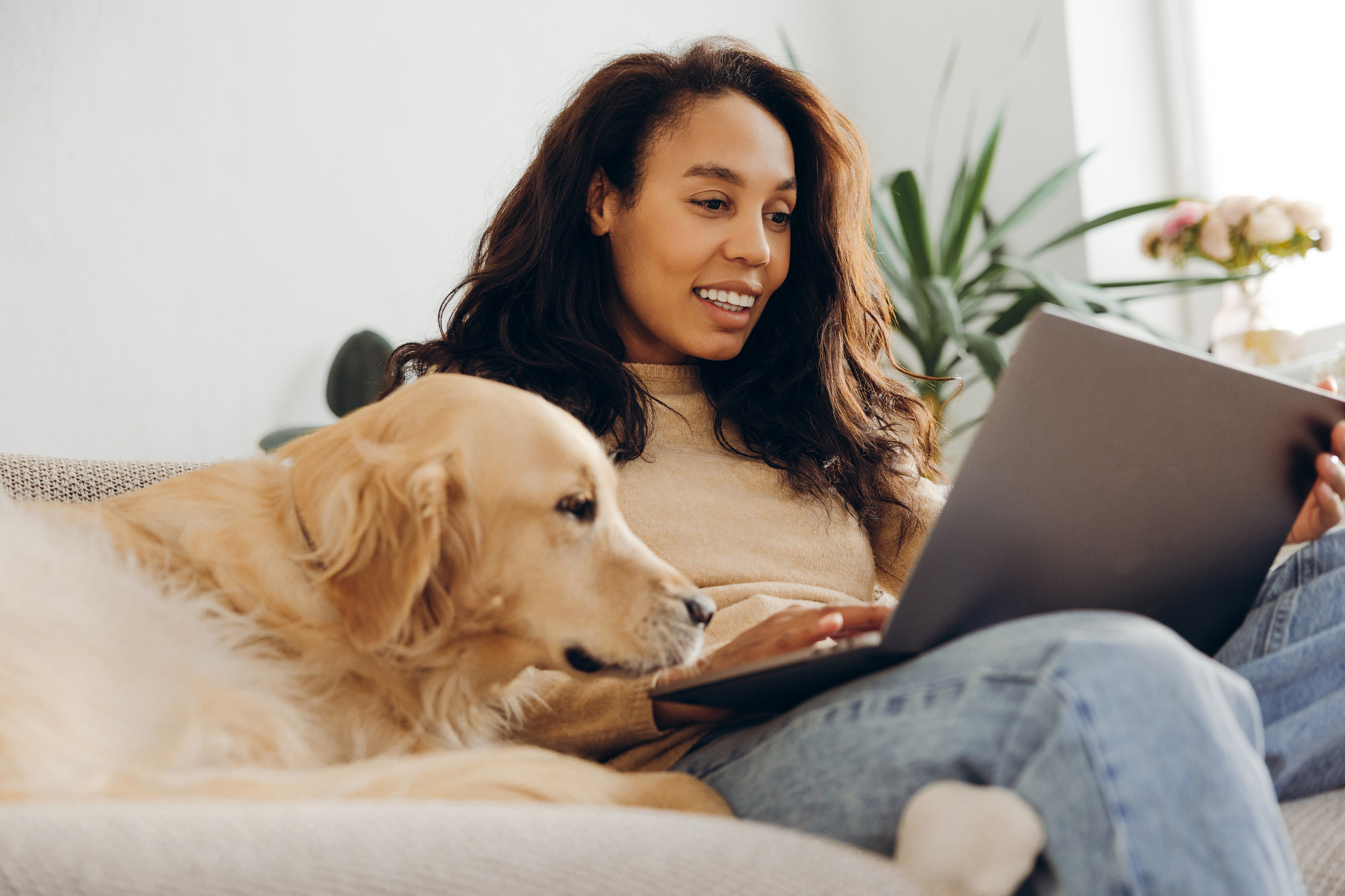 A young woman works on her laptop while sitting on the couch next to her Golden Retriever for Google-Ads-for-pet-care blog.