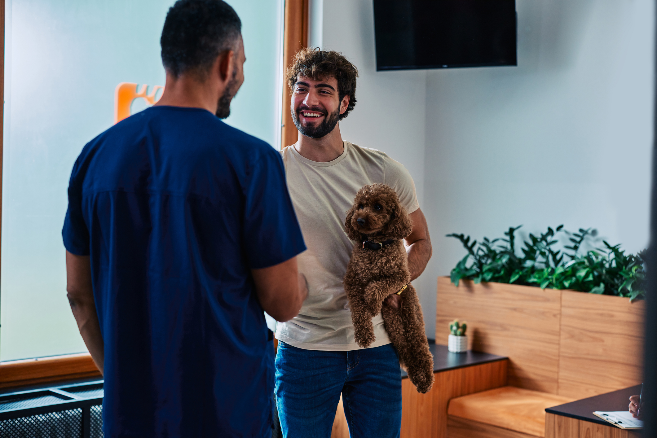 A man holding a poodle speaks to a pet care professional in a facility for pet-care-differentiators blog.